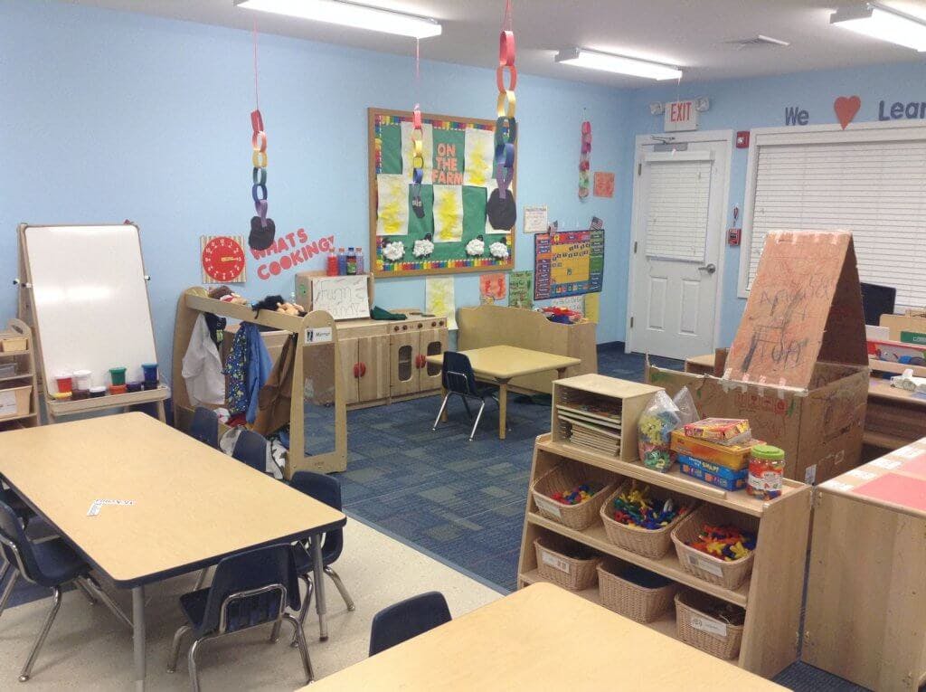 Empty classroom with small tables and chairs, storage shelves, and a whiteboard