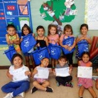 Group of children holding blue bags and white papers