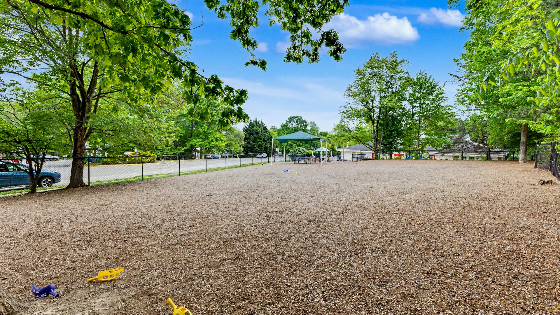 An empty playground with wood chips and a green canopy over a picnic table