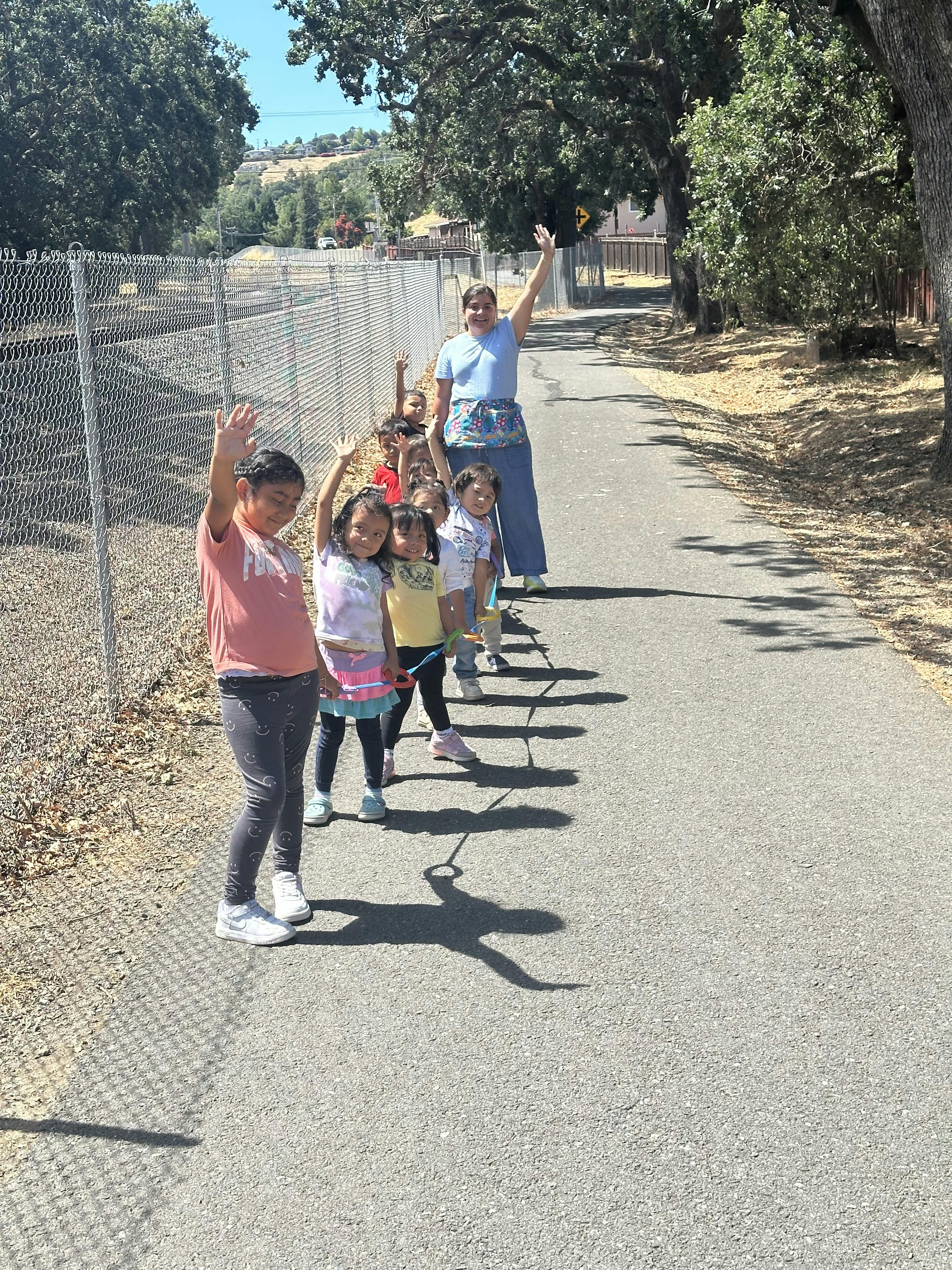 Adult and children walking in a line on a path, all waving