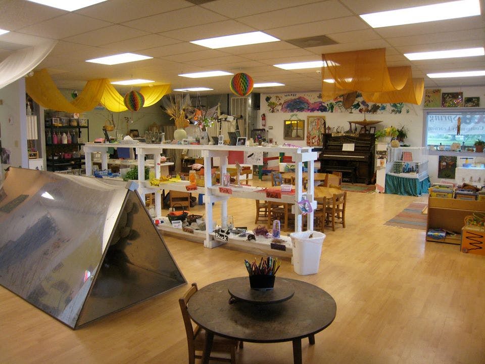 Classroom with shelves of items, small tables and chairs, and a piano