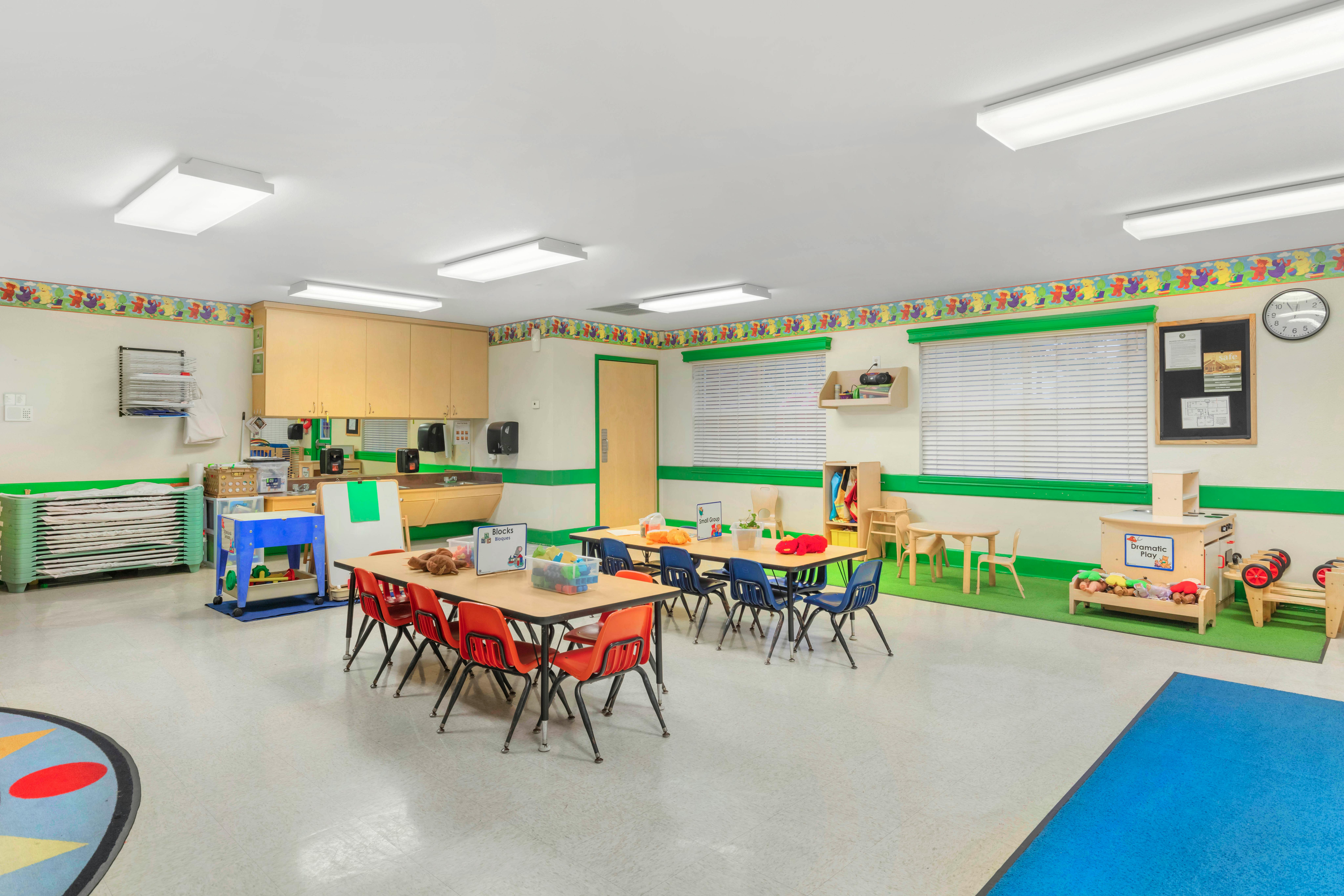Classroom with child-sized tables and chairs, play kitchen, and colorful rug