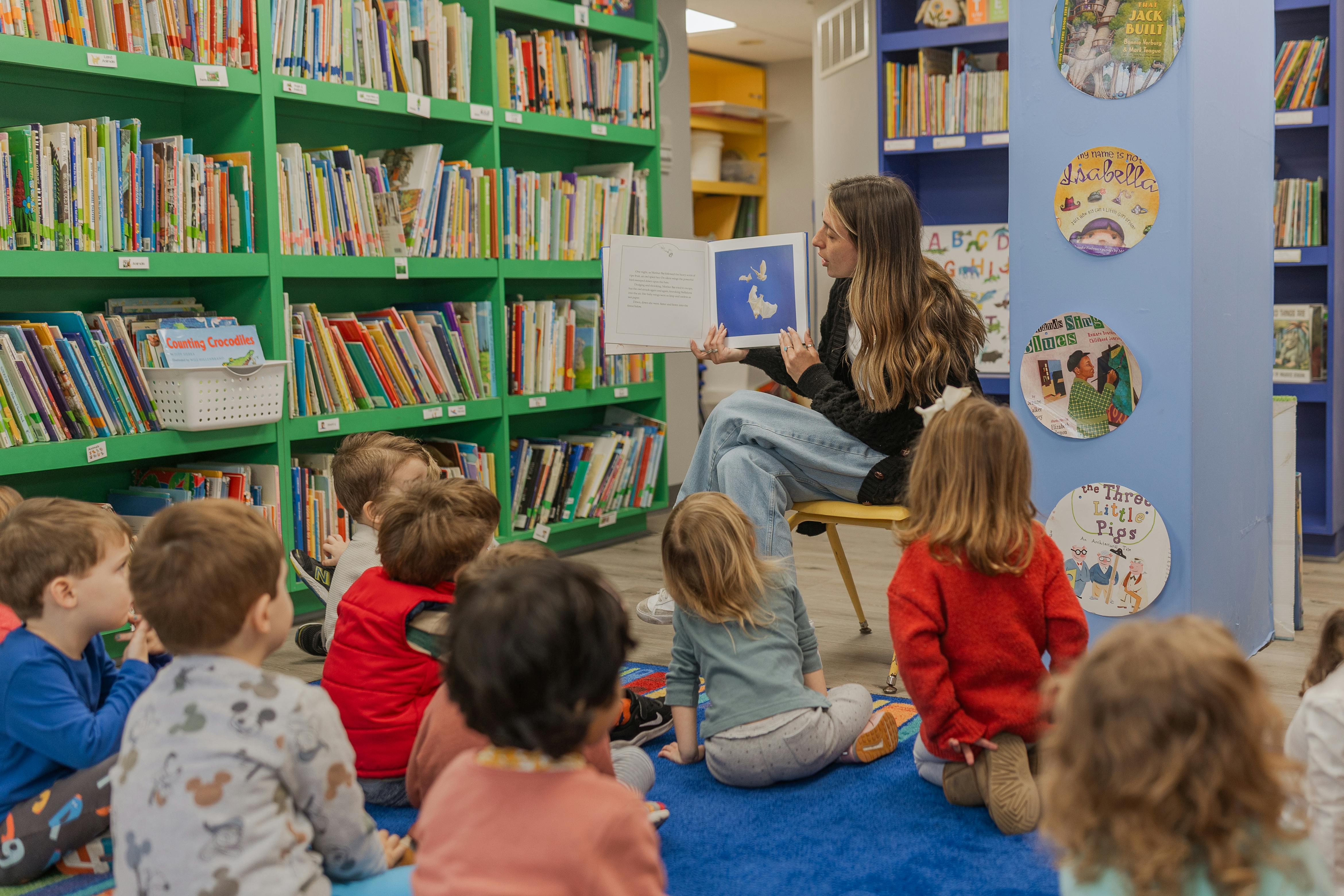 Person reading a book to a group of children in a library