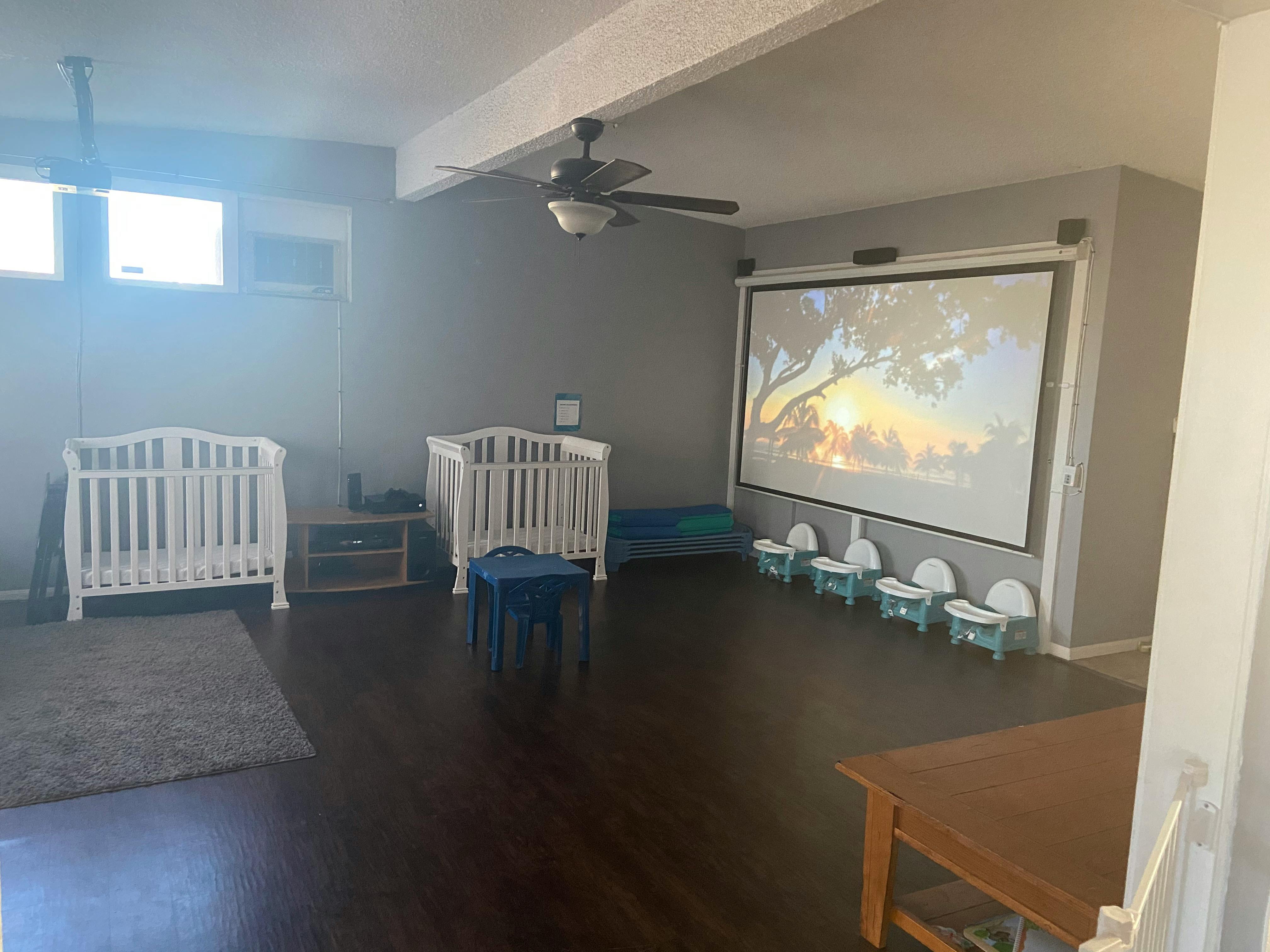 Room with two cribs and a large projection screen showing a nature scene