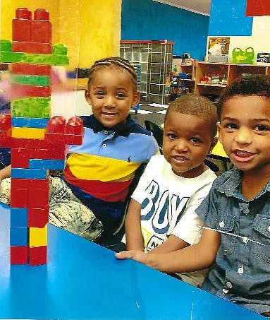 Three children sitting at a table with a block tower
