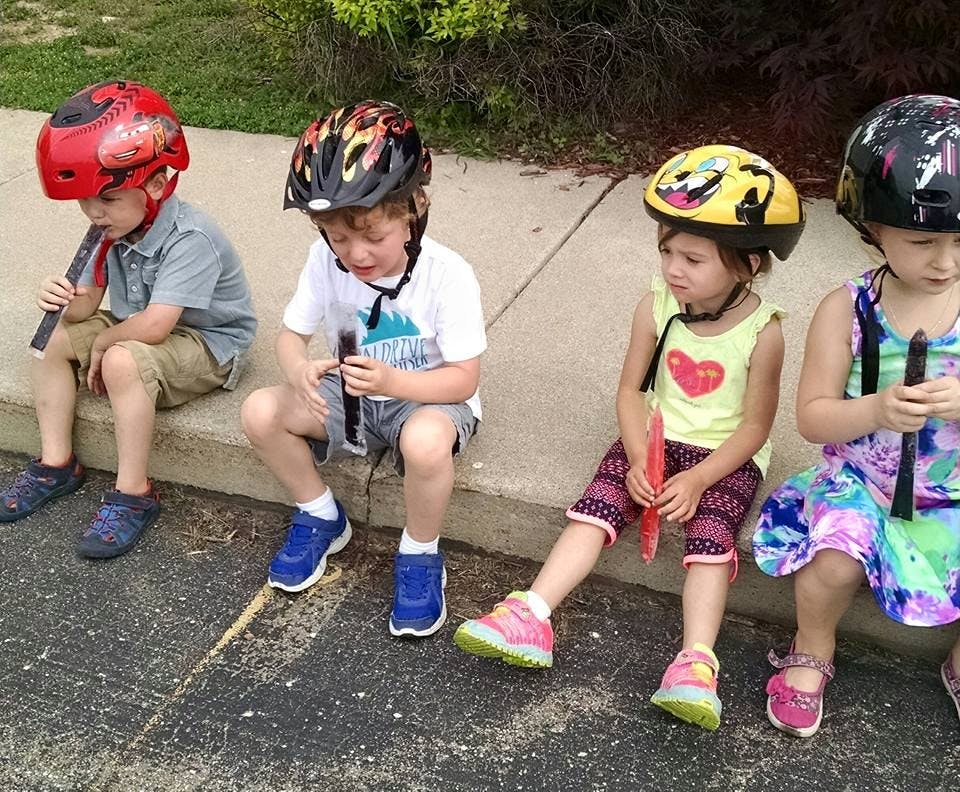 Four children wearing helmets sitting on a curb