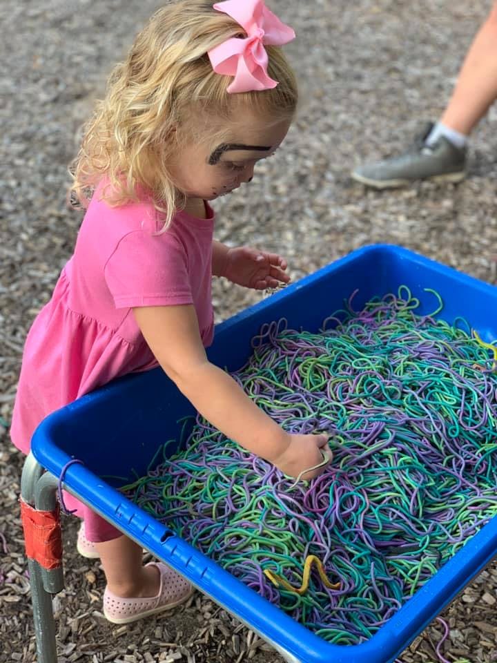 Child playing with colorful strings in a blue bin