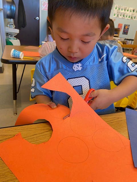 Child cutting orange paper with scissors in a classroom