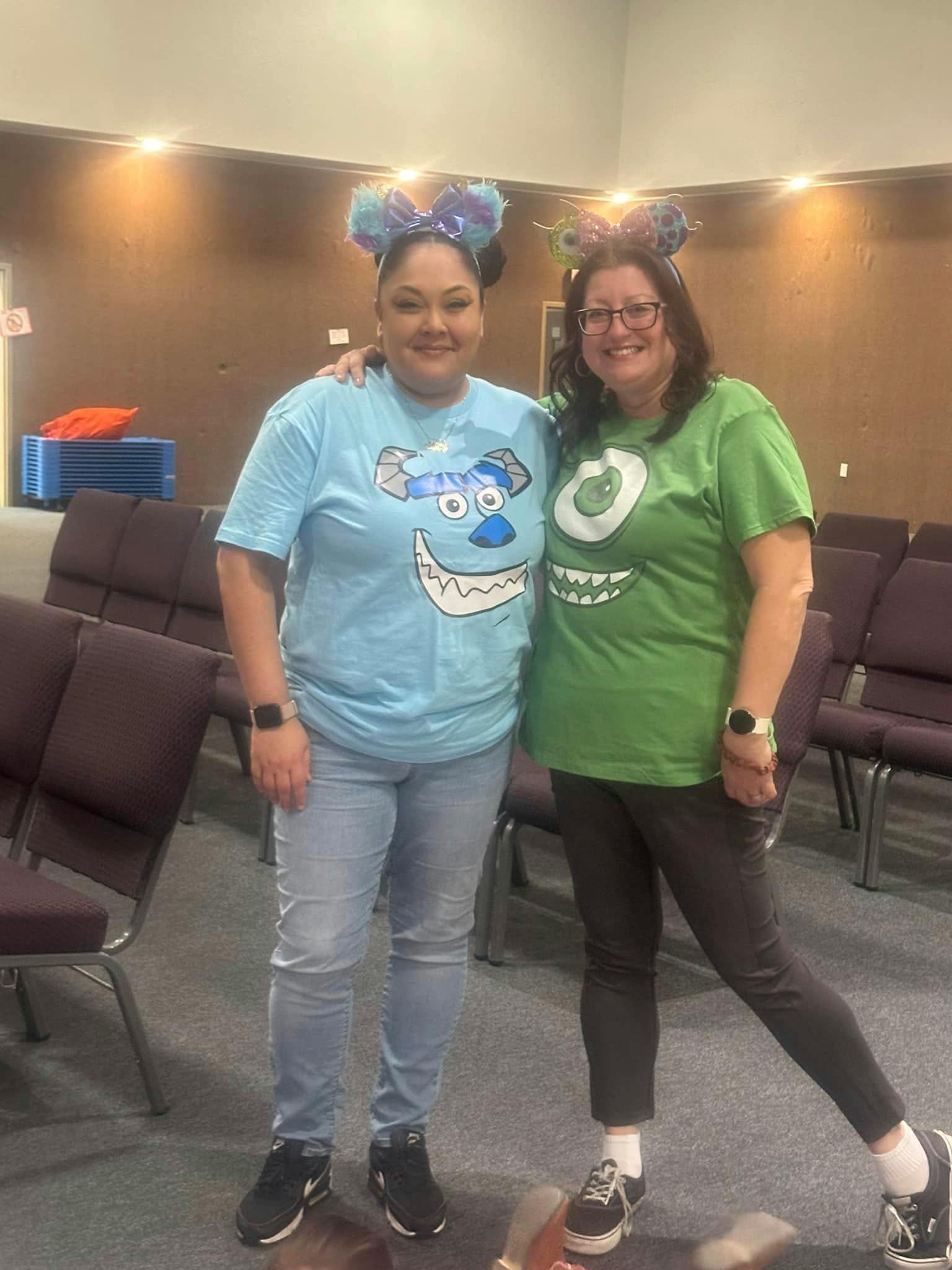 Two people wearing themed shirts and headbands standing in a room with chairs