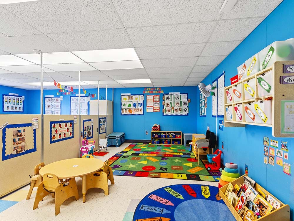 Childcare classroom with small tables, chairs, colorful rugs, and wall decorations