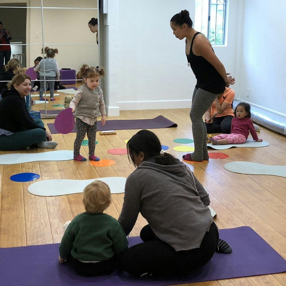 Adults and children in a room with yoga mats and colorful floor markers