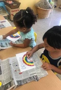 Two children painting rainbow pictures at a table