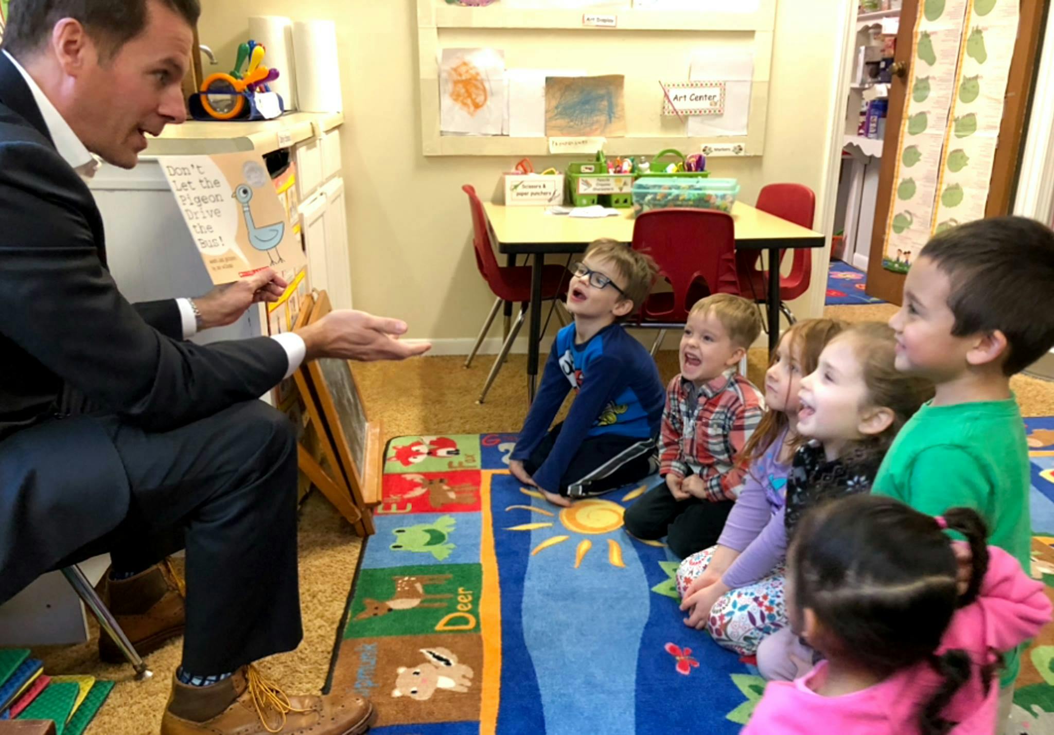 Person reading a book to a group of children in a classroom