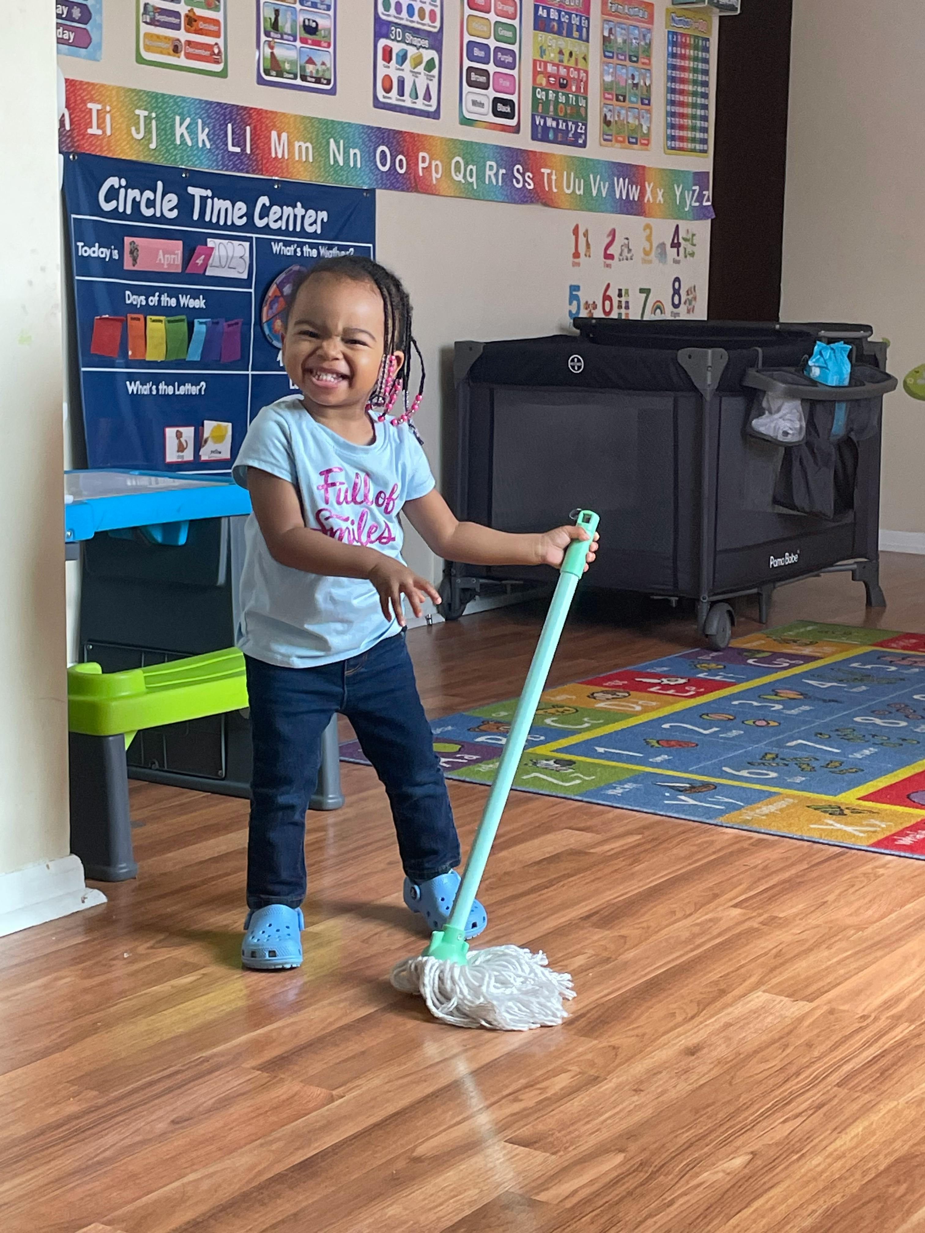 Child holding a mop in a classroom
