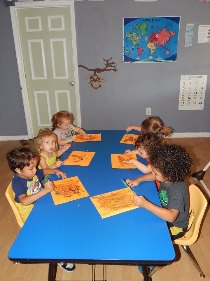 Children sitting at a table drawing on orange paper