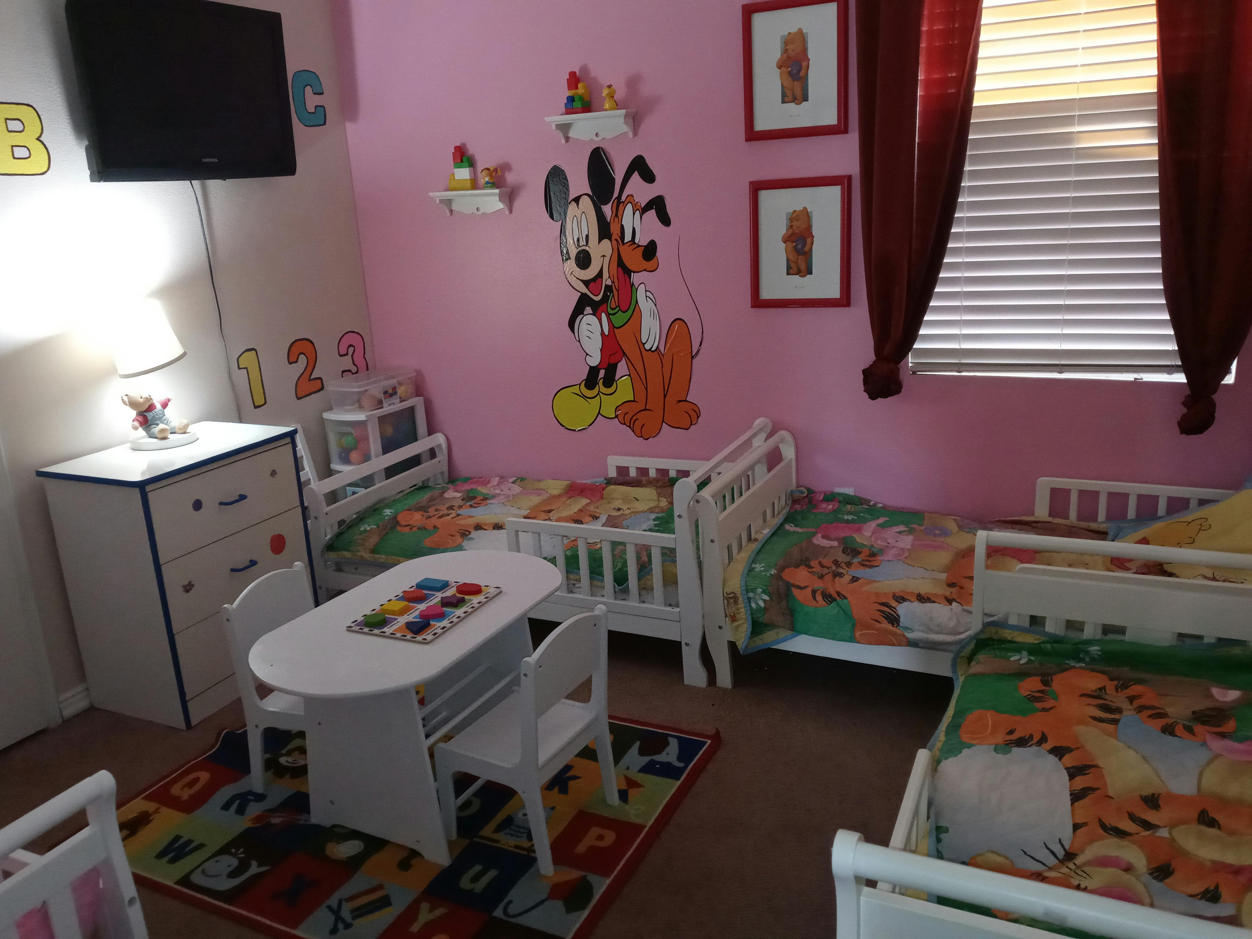 Children's room with multiple cribs, a small table and chairs, and wall decorations