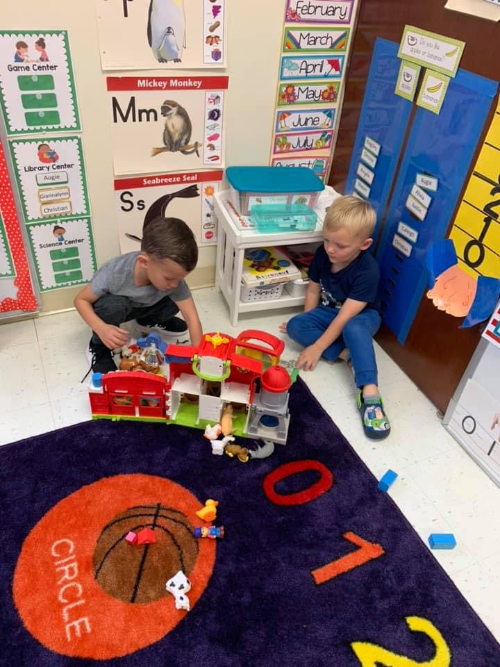 Two children playing with toys on a rug in a classroom