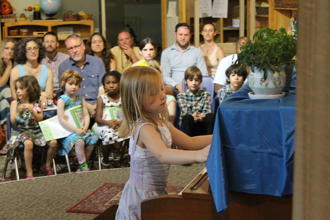 Child playing piano with people watching in background