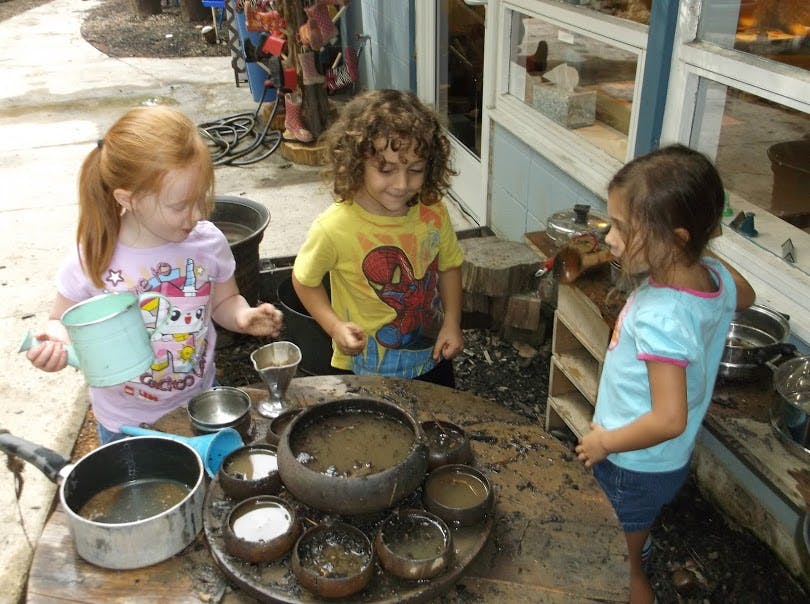 Three children playing with pots and pans outdoors