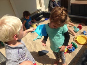 Two children playing in a sandbox with sand toys