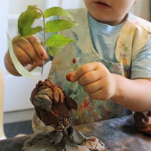 Child in apron working with clay and a plant stem