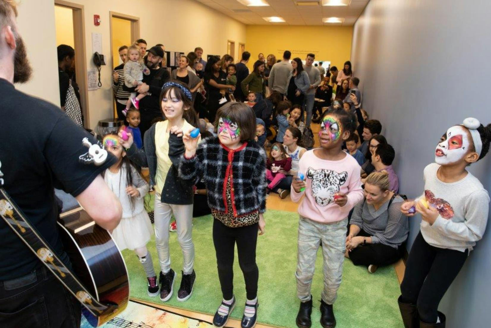 Person playing guitar for children with painted faces