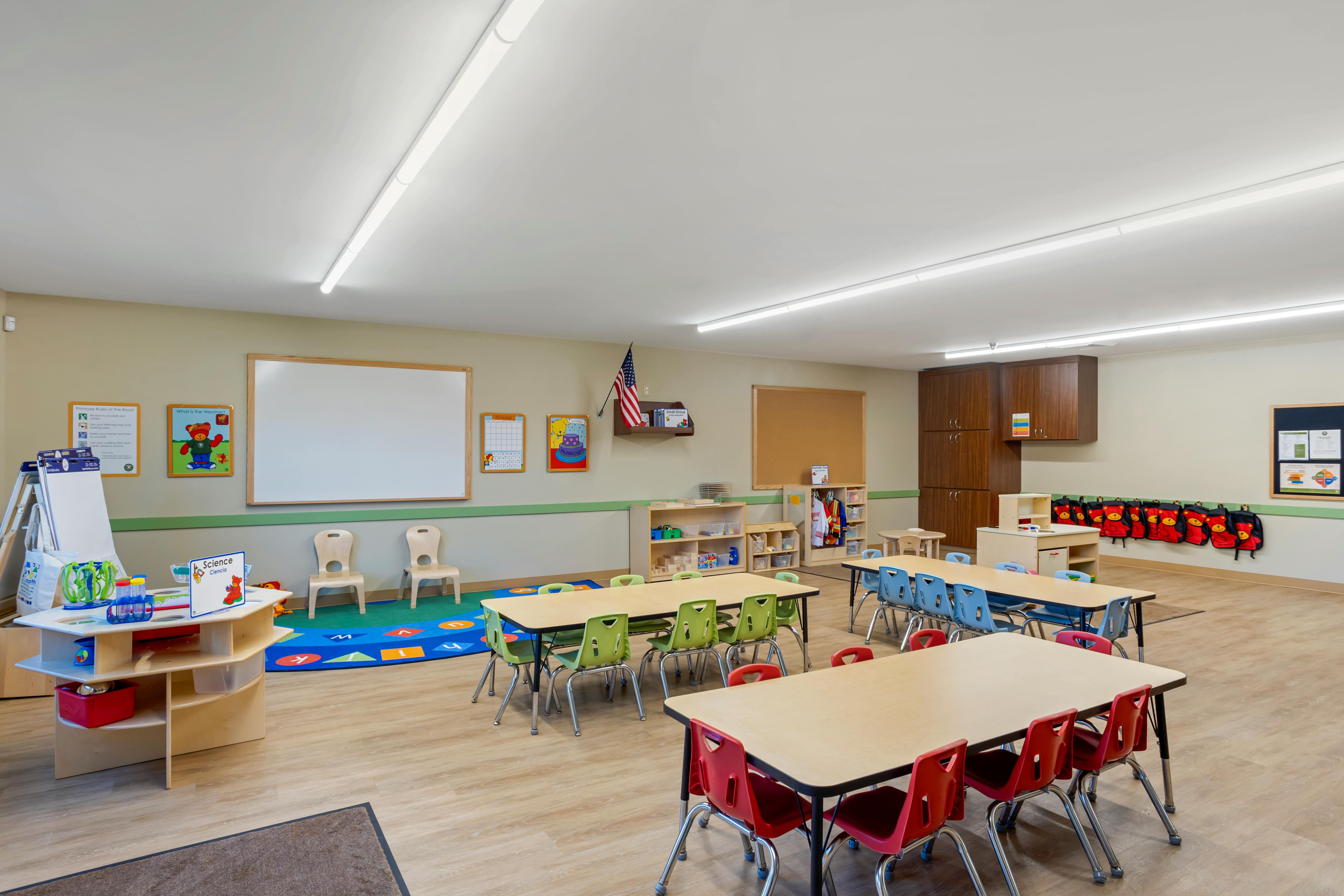 An empty early childhood classroom with colorful tables, chairs, and learning stations