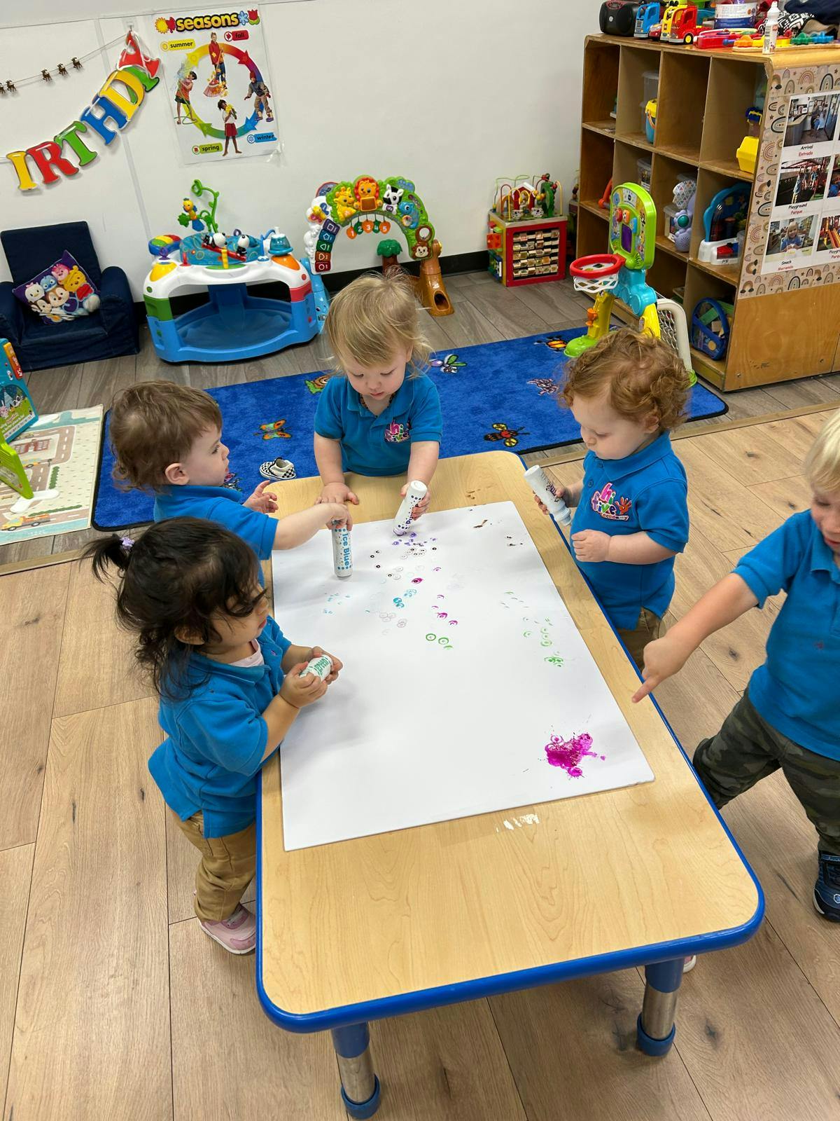 Several young children painting on a large sheet of paper at a table