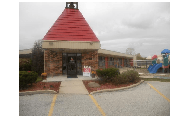 Entrance of a building with a red roof, brick facade, and a playground nearby