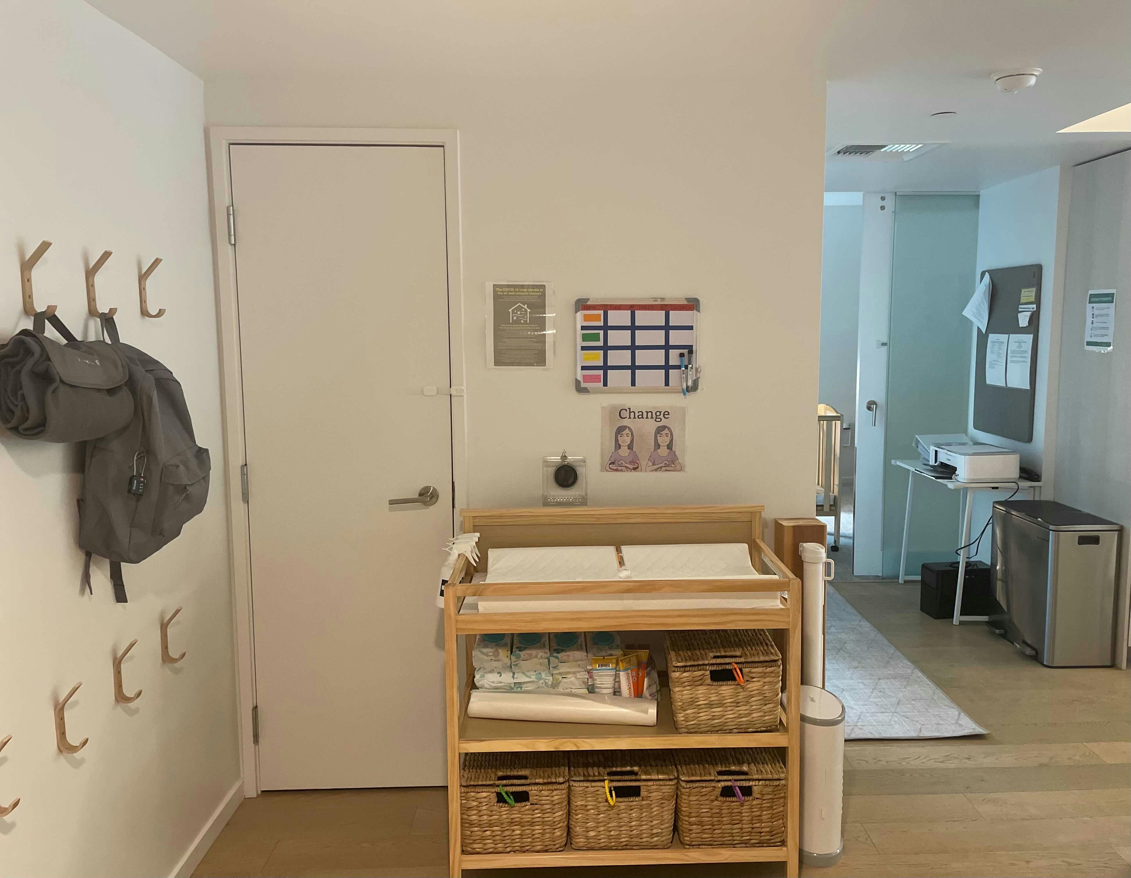 Changing table with baskets and supplies in a room with a backpack on hooks