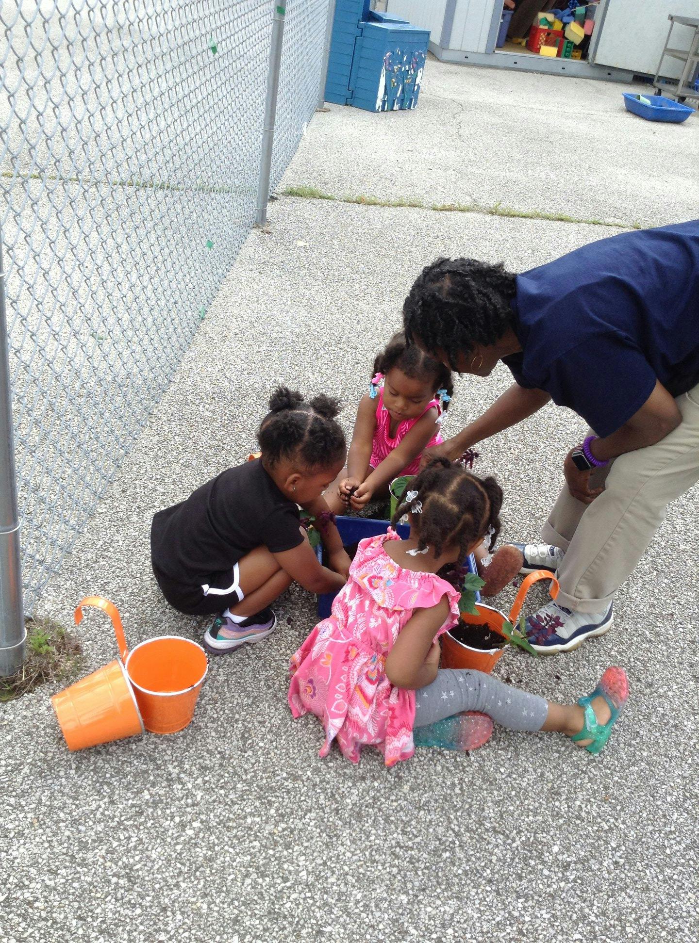 Adult and three children planting in small pots on the ground