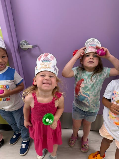 Three children wearing paper hats and holding small objects