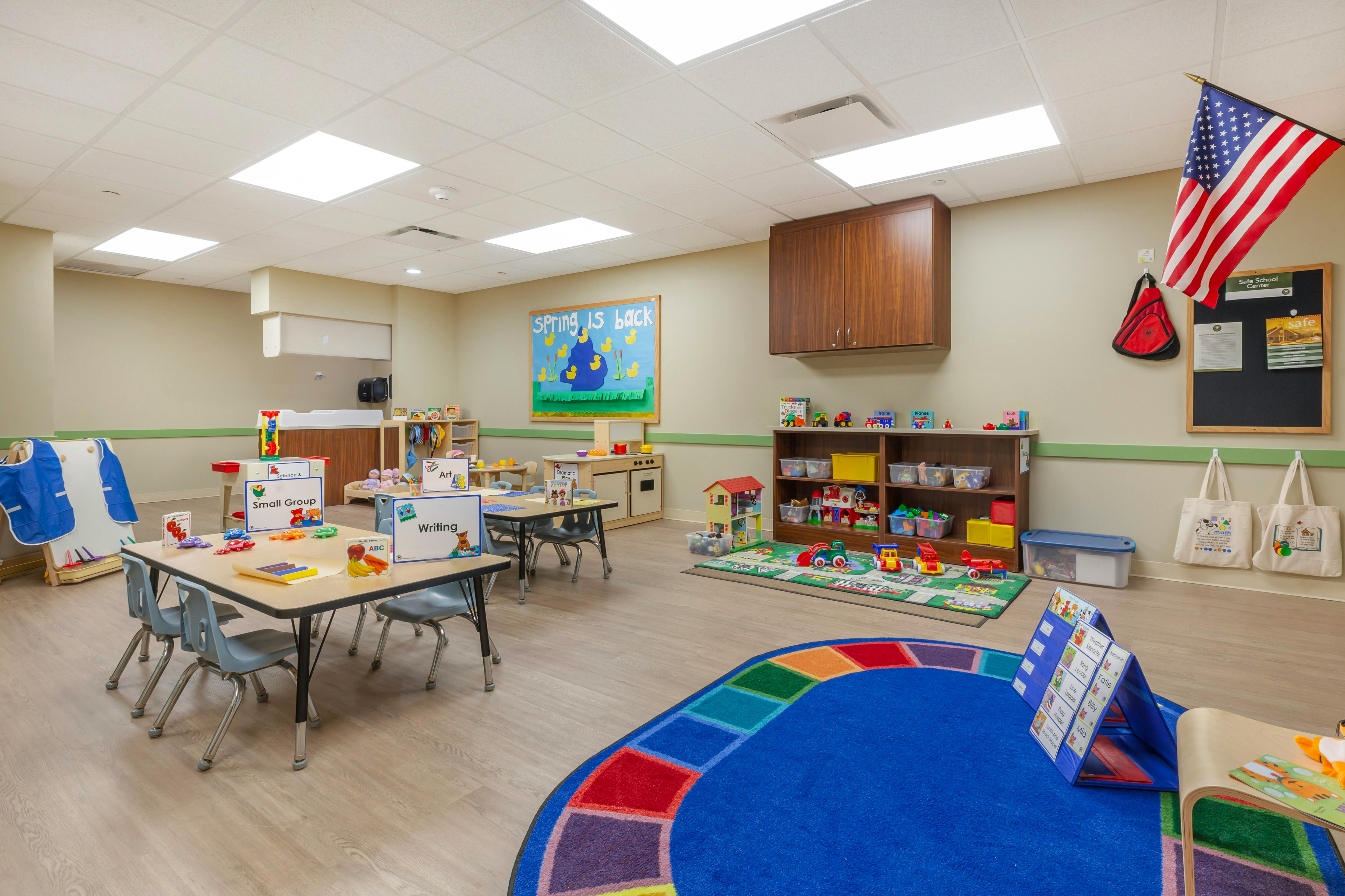An empty early childhood classroom with tables, chairs, toys, and an American flag