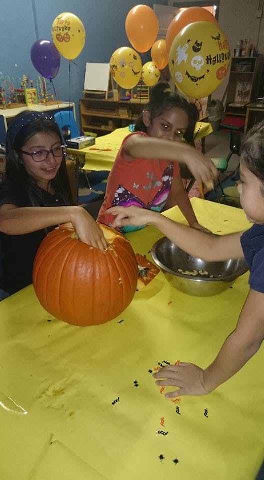 Children carving a pumpkin on a yellow table