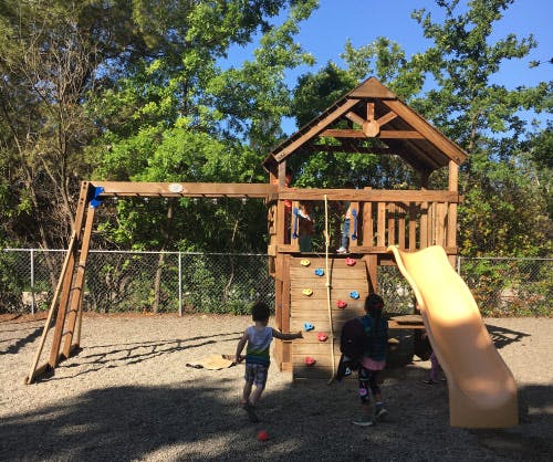 Children playing on a wooden playground structure with a slide