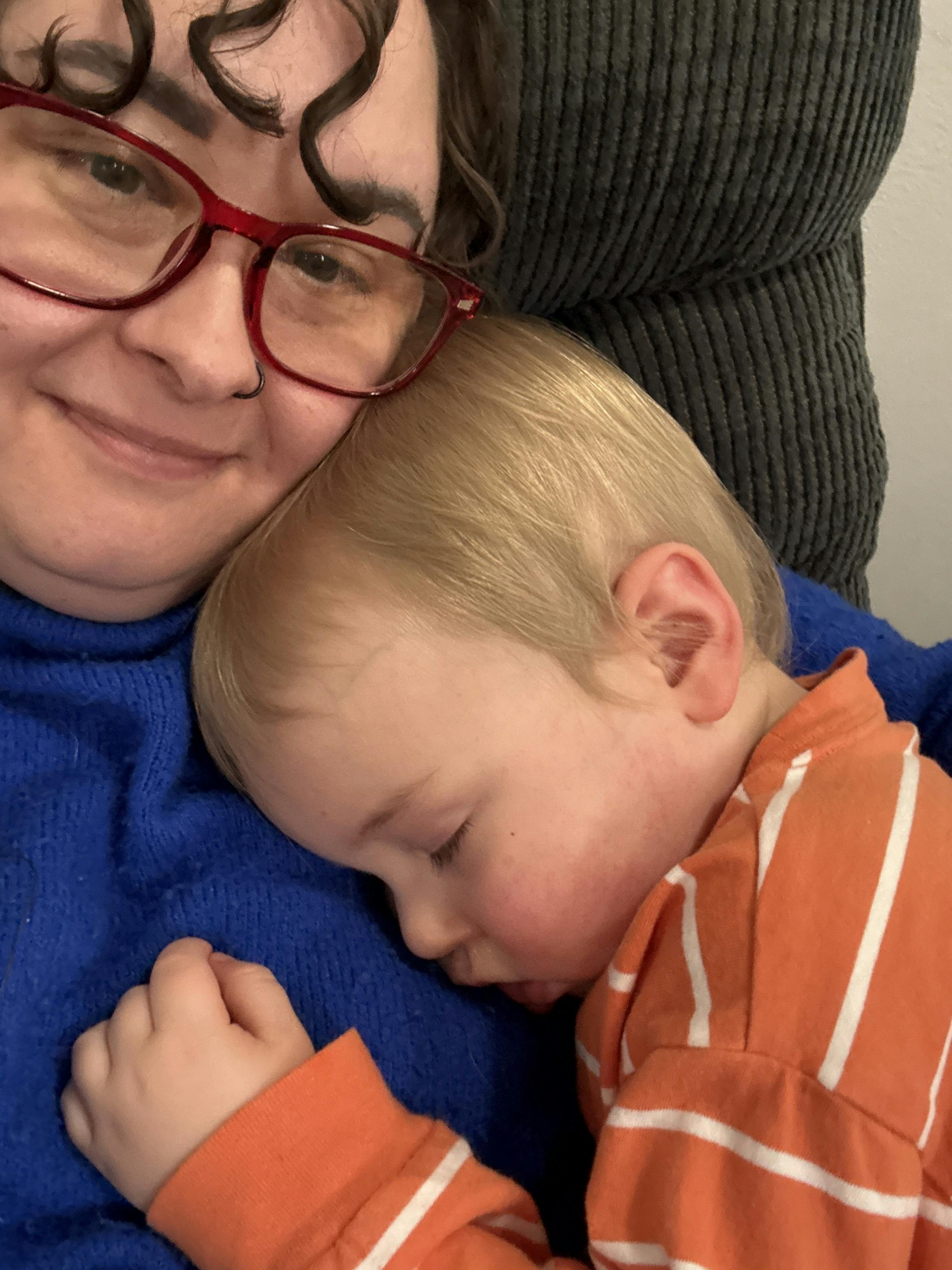 Person wearing glasses holding a sleeping child