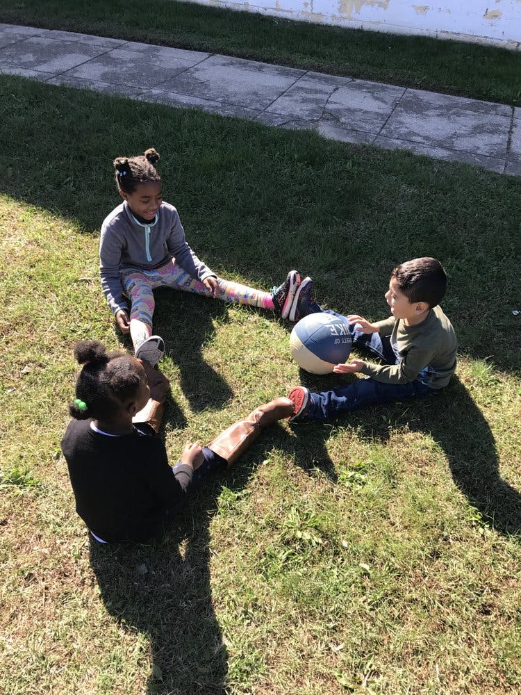 Three children sitting on grass with a ball