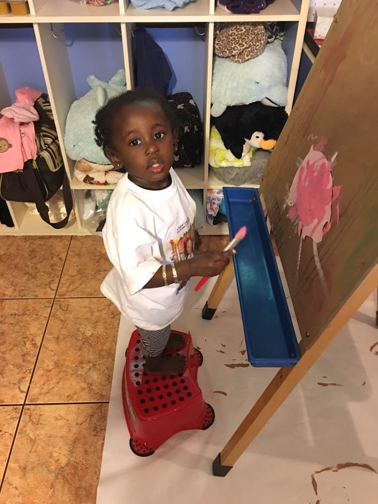Child standing on a red stool painting at an easel