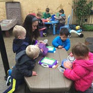 Adult and multiple children gathered around a table outdoors