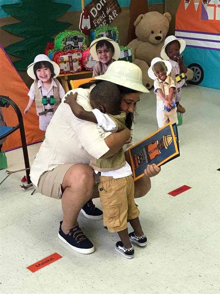 Person in a hat hugging a child while holding a book