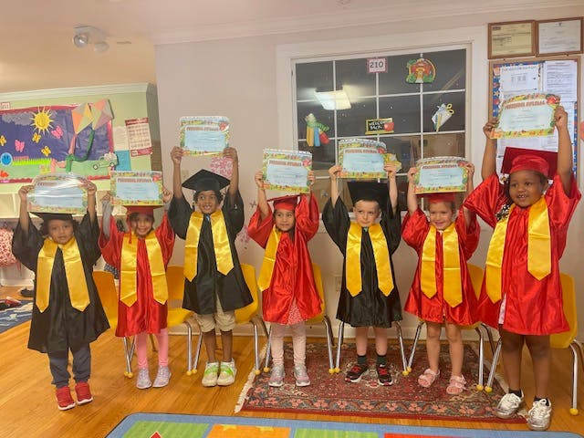 Group of children in graduation caps and gowns holding diplomas in a classroom