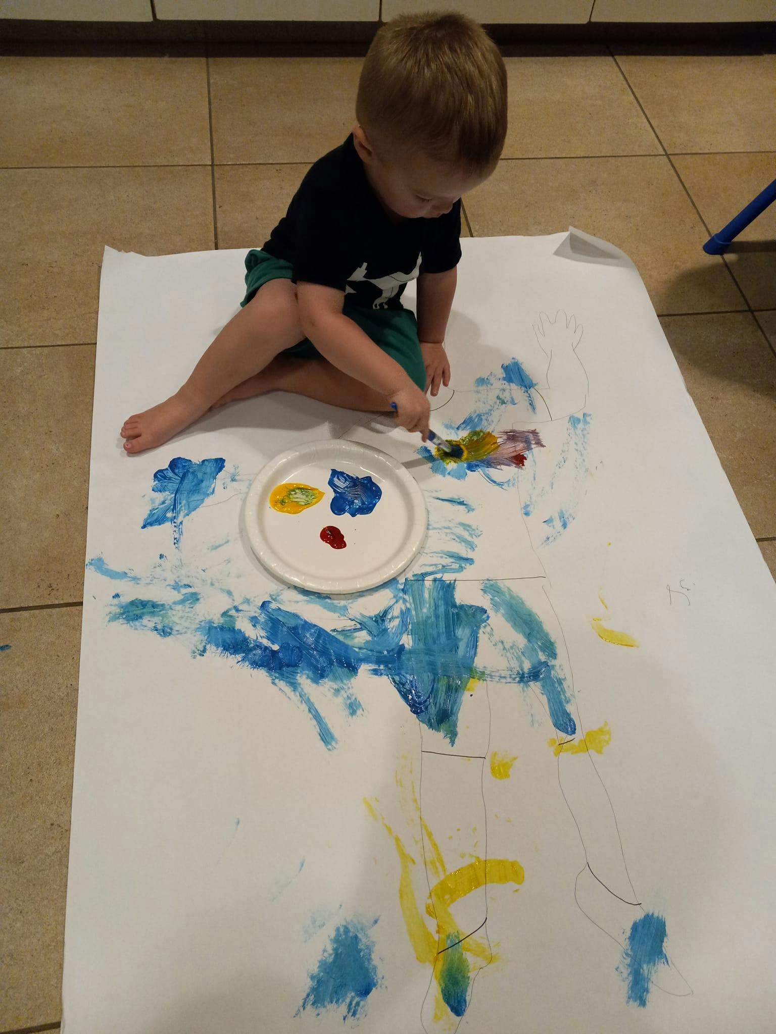 Child sitting on floor painting on large paper