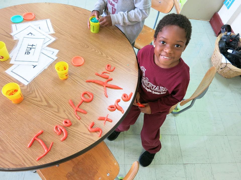 Child standing next to a table with play-doh letters spelling "I go to the store"