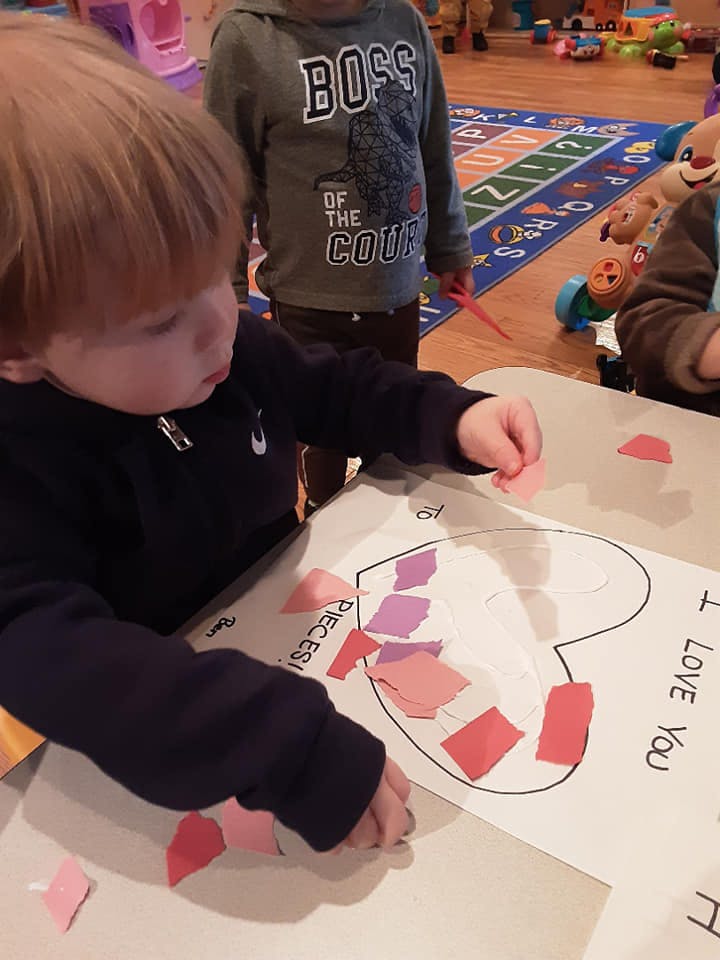 Child doing a craft with paper pieces on a heart outline