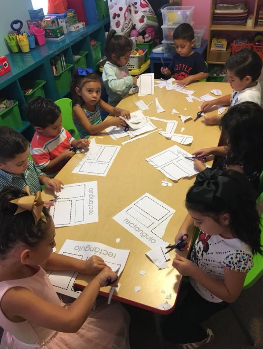 Children cutting paper shapes at a table in a classroom