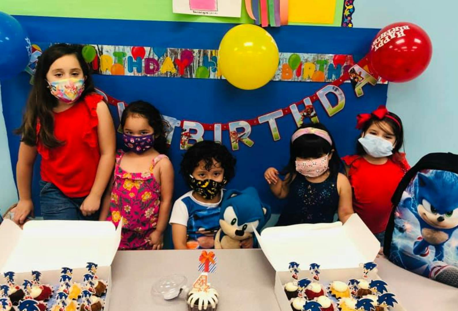 Children wearing masks at a birthday party with cupcakes and balloons