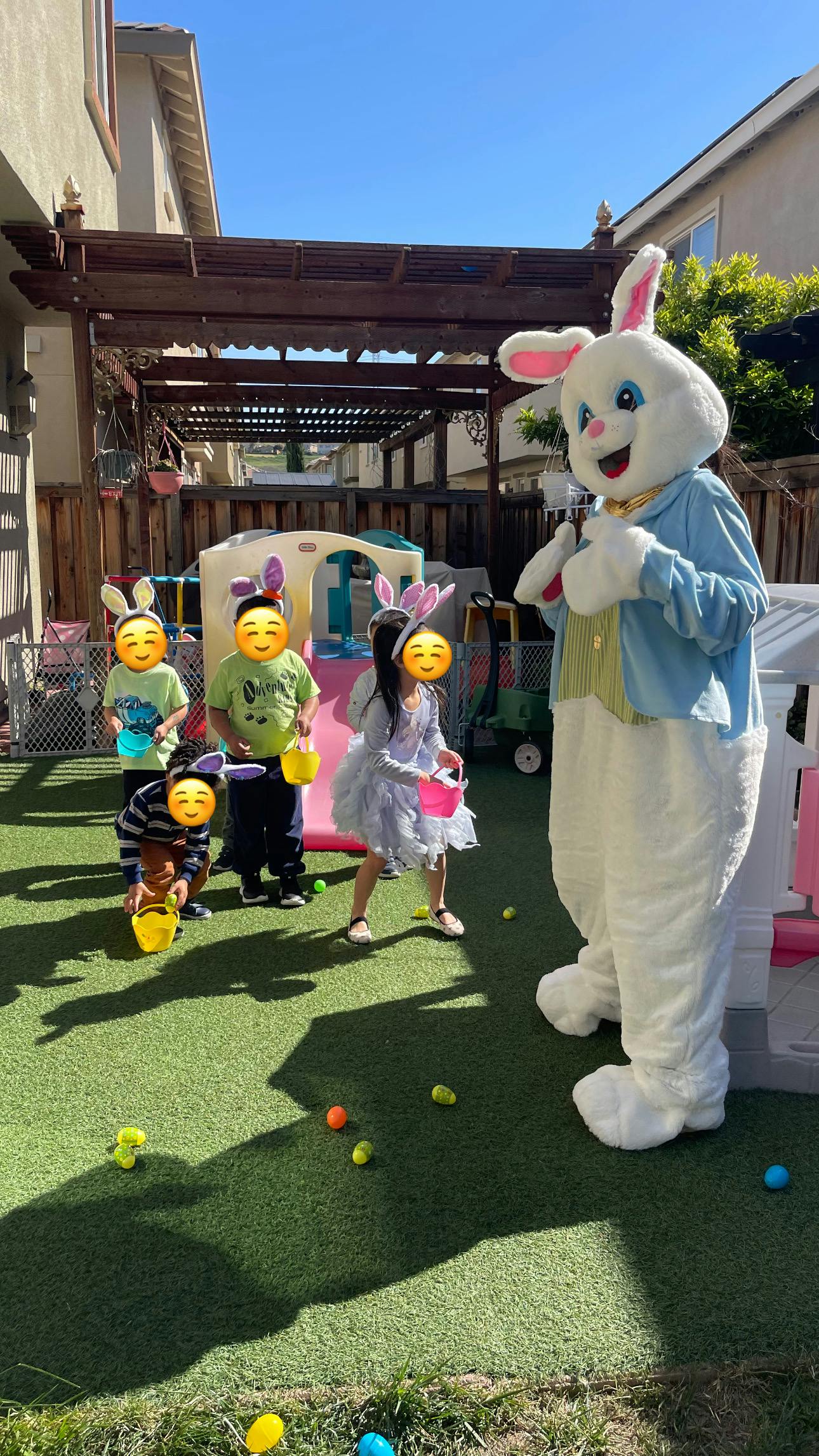 Children with baskets and a person in a bunny costume on artificial grass