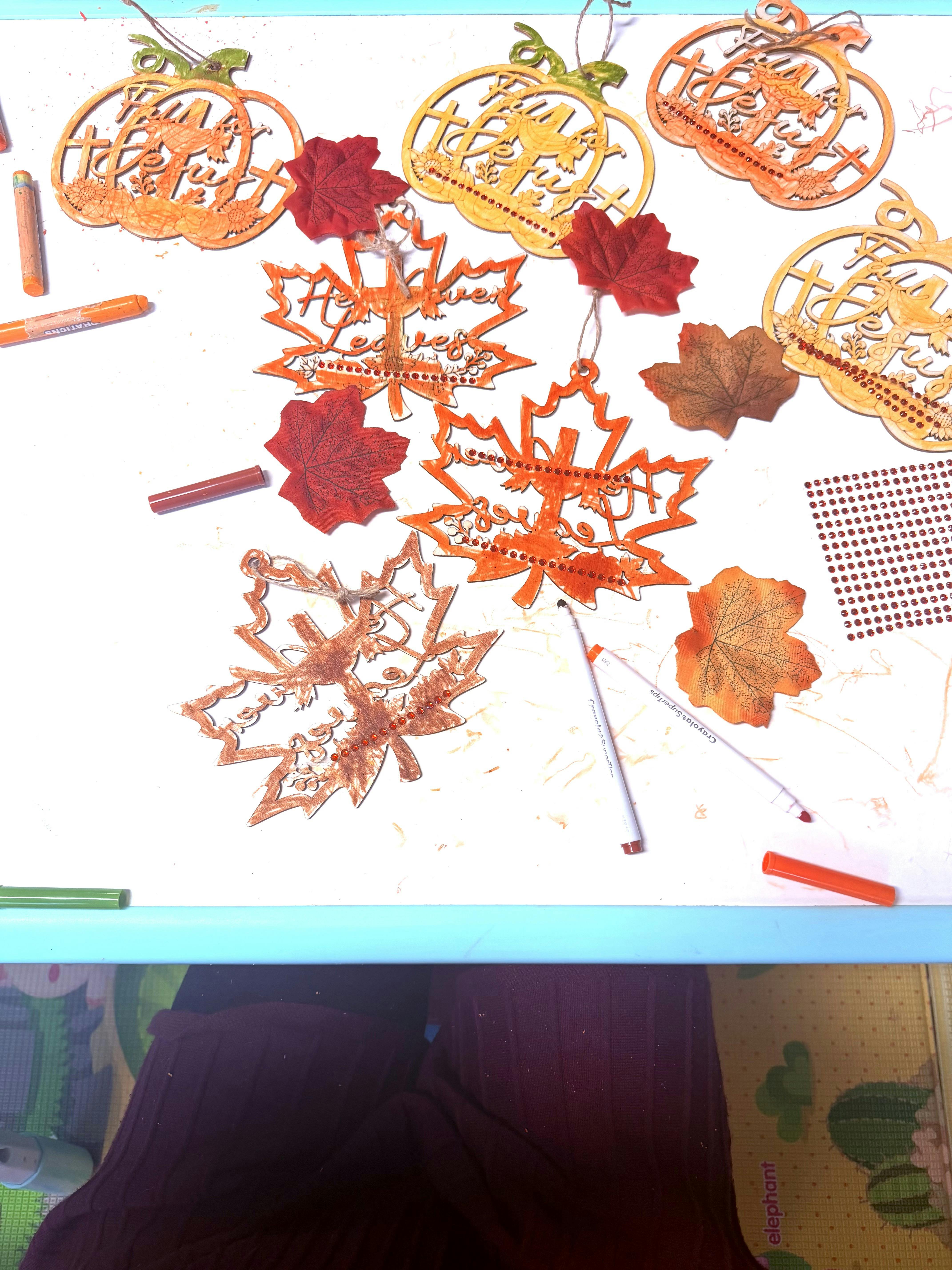 Wooden pumpkin and leaf crafts with markers and rhinestones on a table