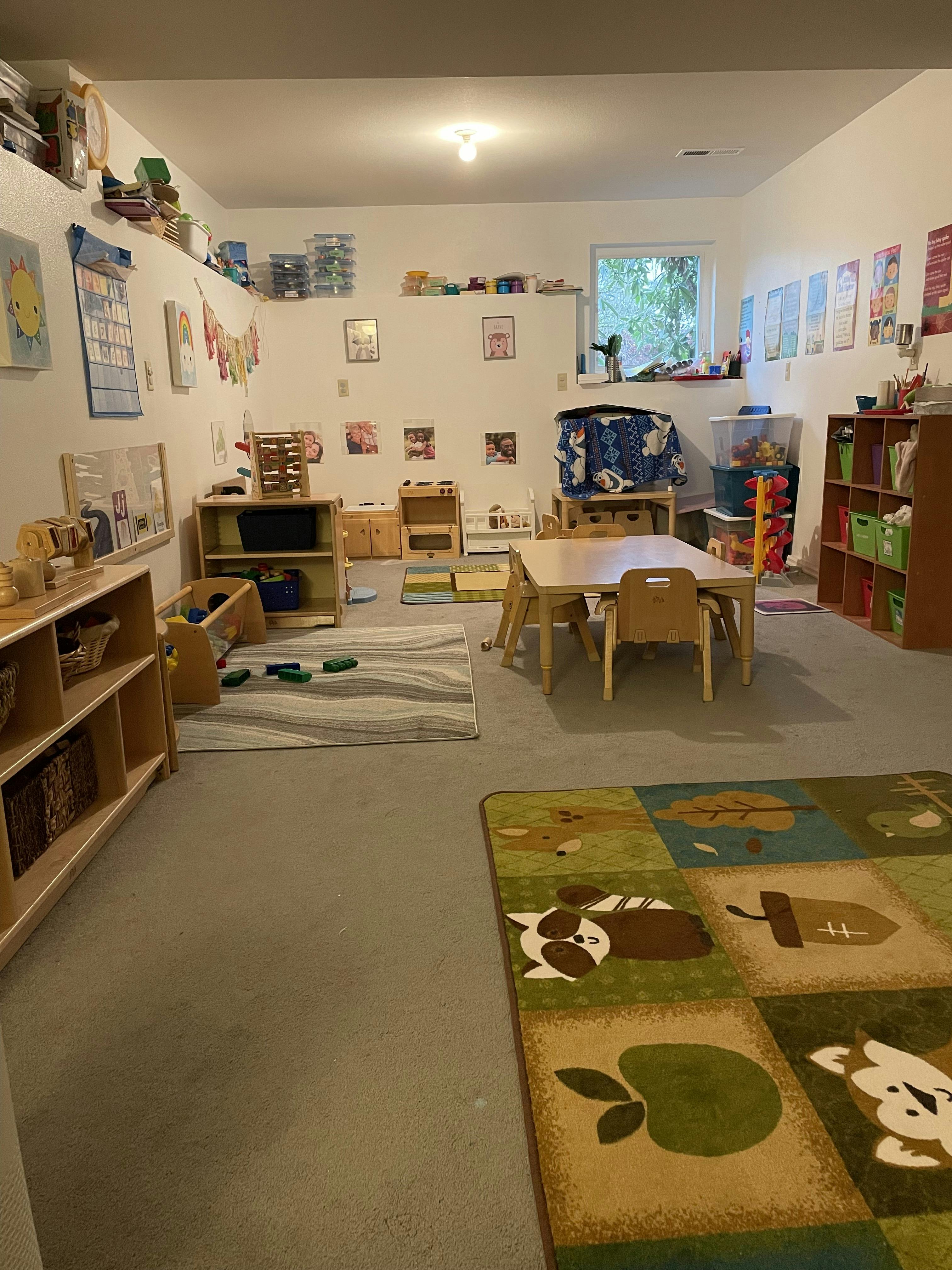 Childcare room with rugs, small tables, chairs, and shelving for toys