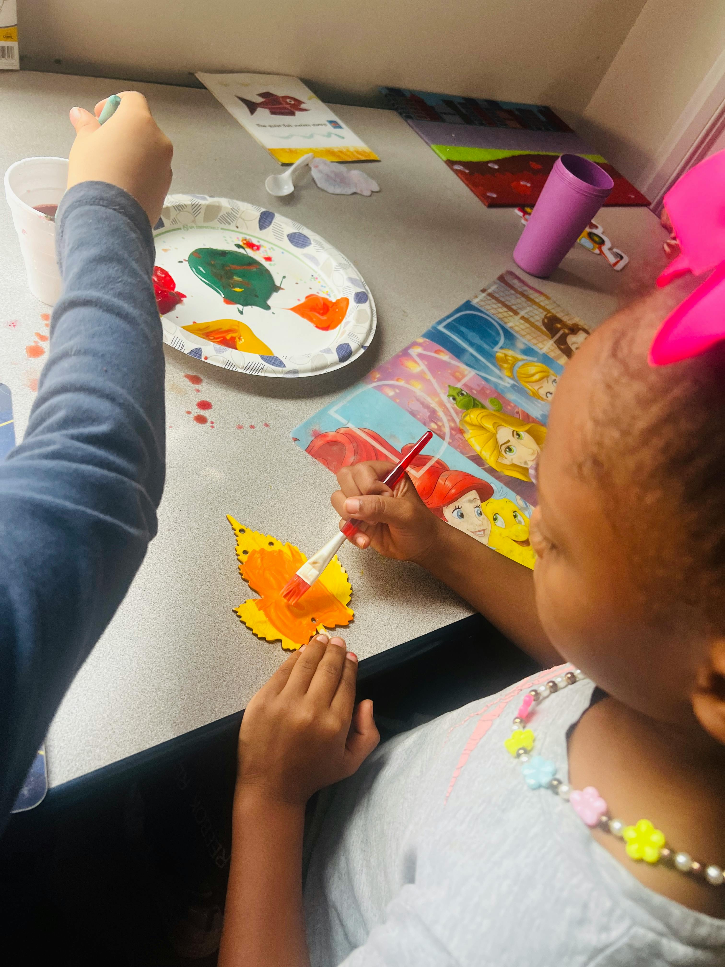 Two children painting leaf cutouts at a table
